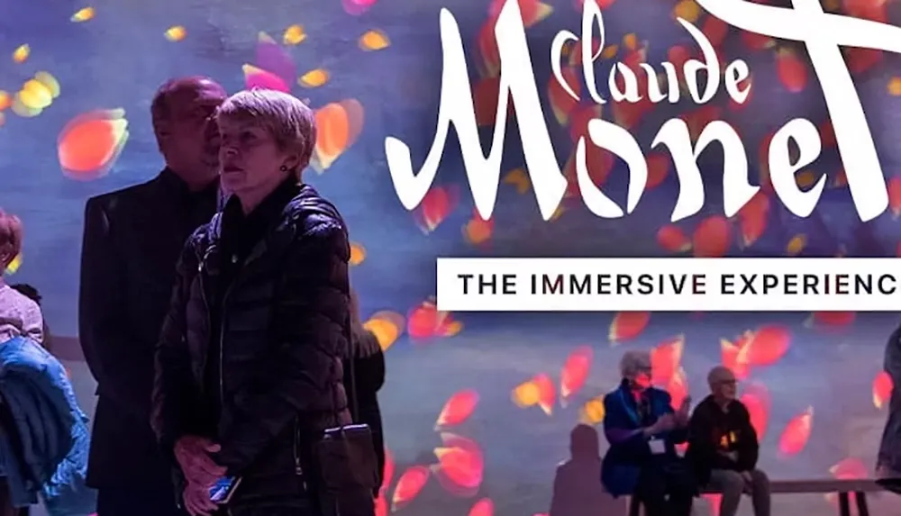 Several people are observing an immersive Monet art experience with colorful abstract projections in the background