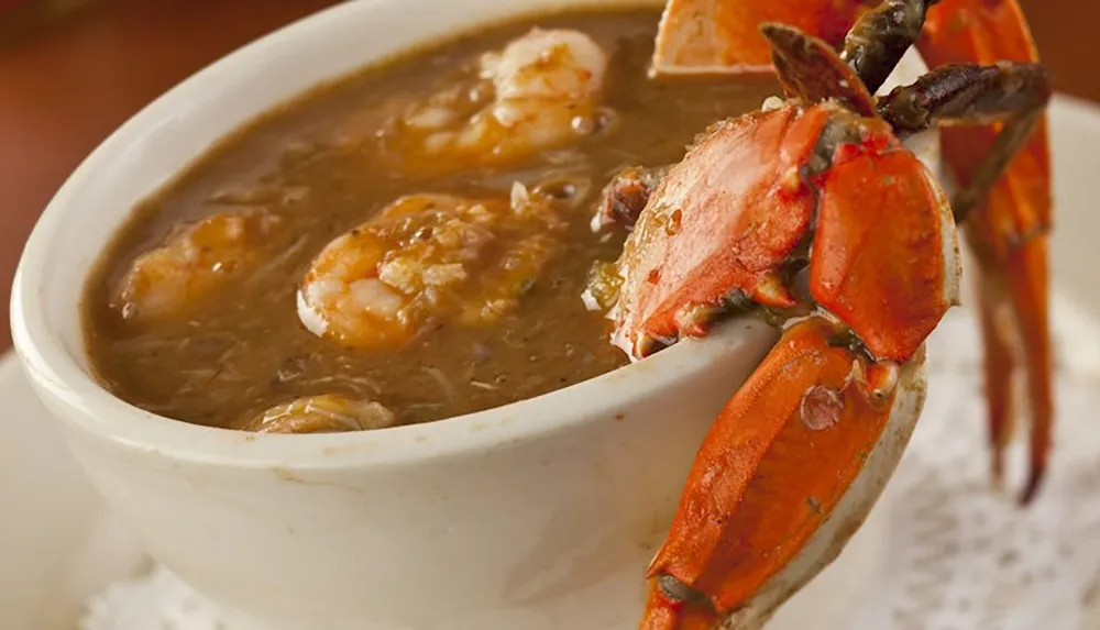 A bowl of seafood gumbo with shrimp and a crab claw garnishing the side