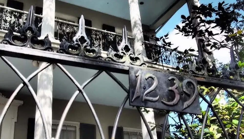 The image shows a wrought iron gate with the house number 1239 in front of a building with ornate balcony railings