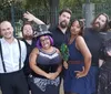 A group of eight people are posing playfully in front of a fence with each expressing a unique and humorous gesture