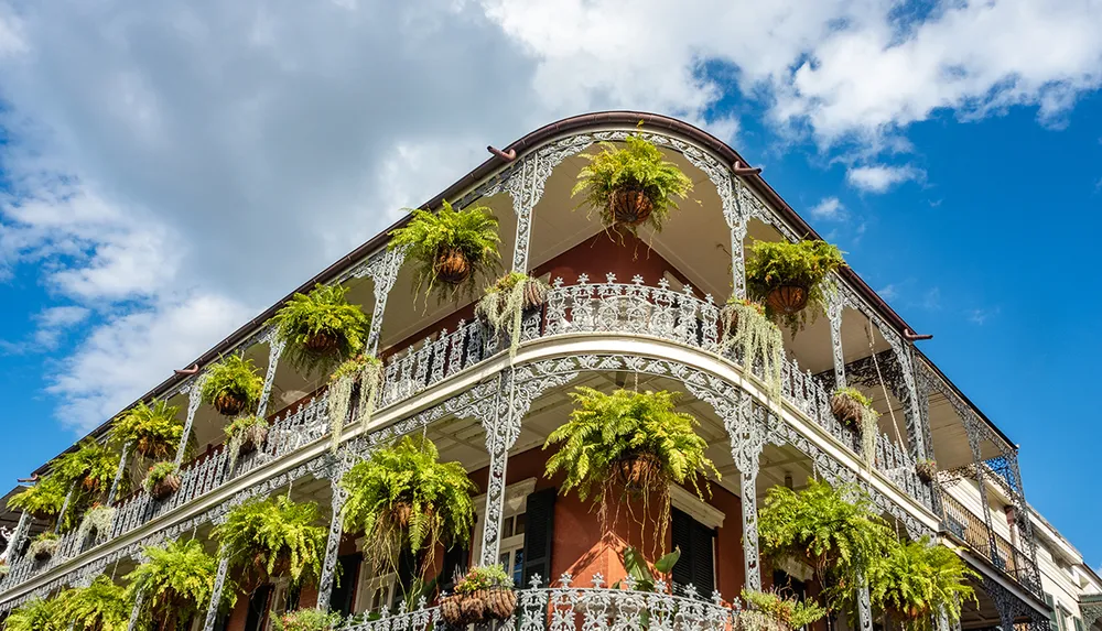 The image shows a historic building with ornate wrought iron railings and lush hanging plants set against a blue sky with clouds