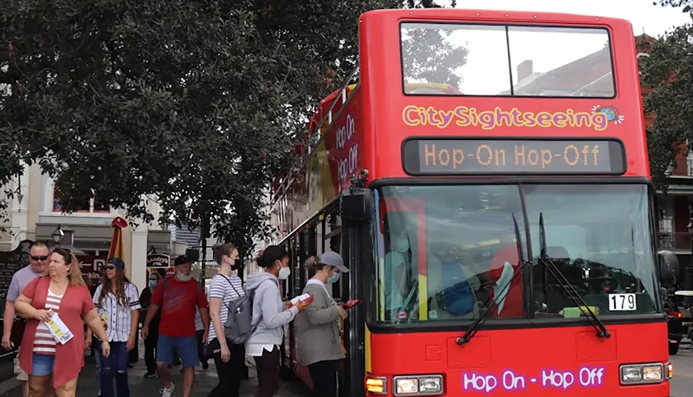 A group of people are walking by a red double-decker CitySightseeing bus with a Hop-On Hop-Off sign