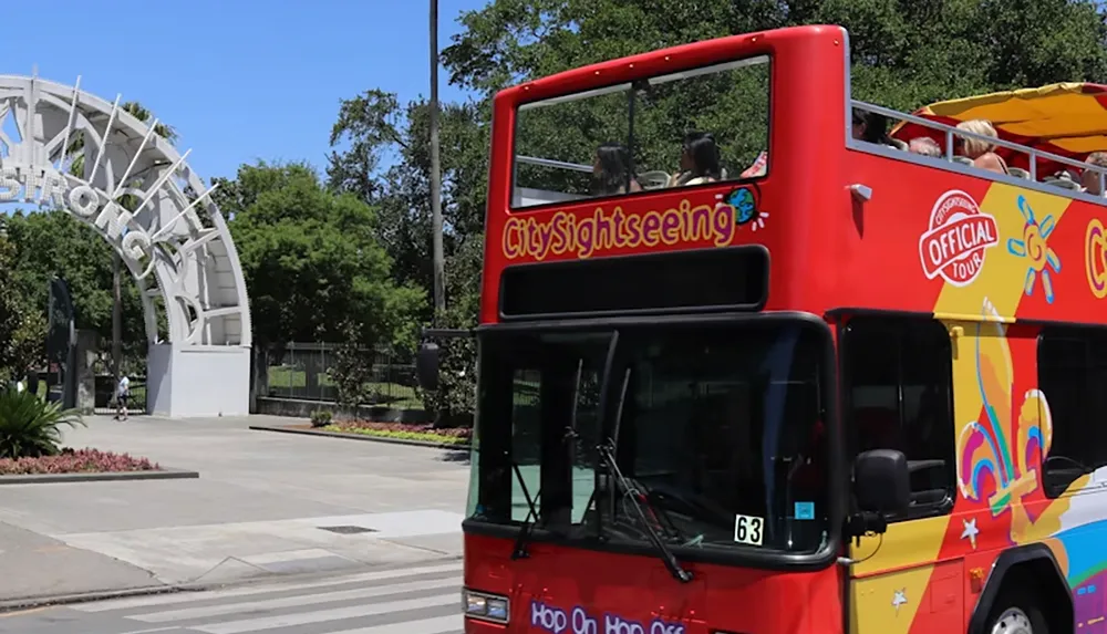 A vibrant red City Sightseeing double-decker bus passes by an arched entrance with greenery in the background