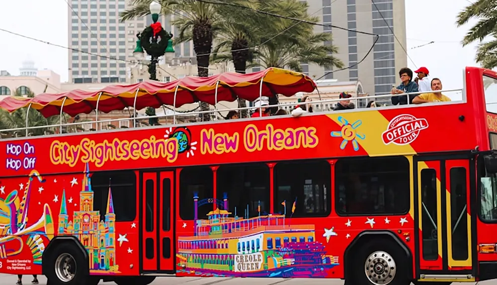 The image shows a colorful double-decker City Sightseeing bus in New Orleans with an open top deck and passengers onboard surrounded by palm trees and city buildings