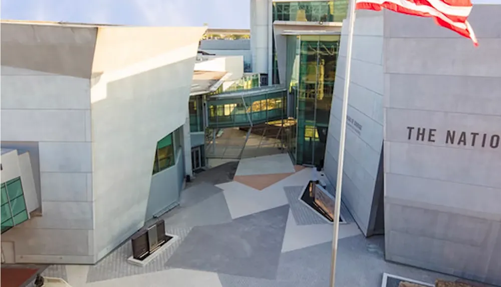 The image shows a modern building with angular architecture featuring large glass sections and an American flag pole in the foreground