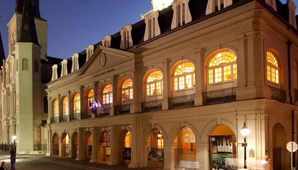 The image shows a historic building with illuminated arched windows and a prominent tower at dusk