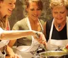 Three women wearing aprons are happily cooking together stirring and adding ingredients to a pot