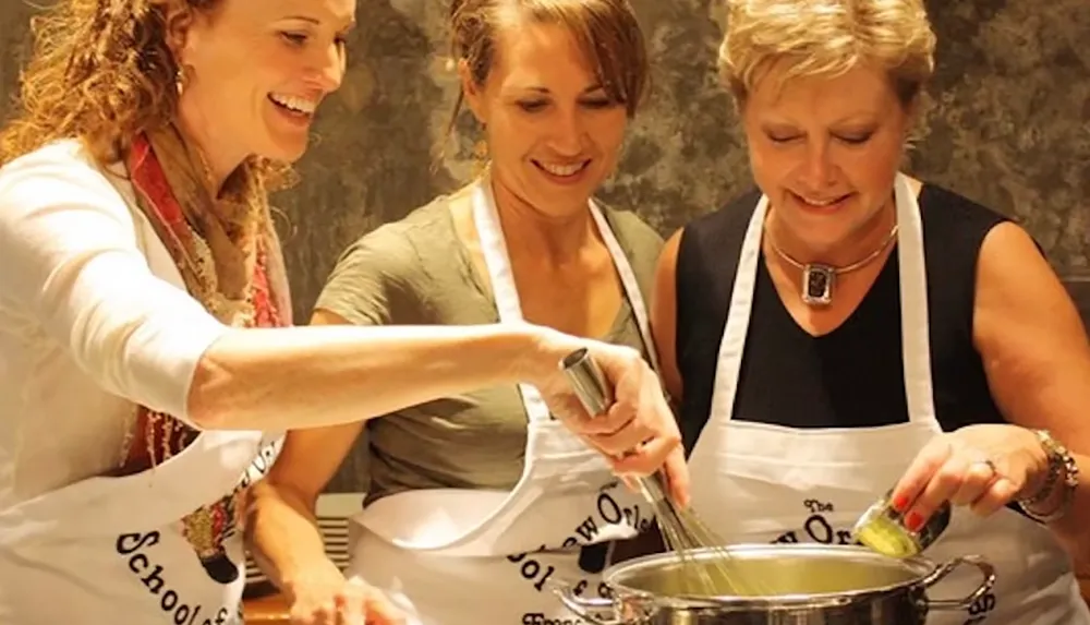 Three women wearing aprons are happily cooking together stirring and adding ingredients to a pot