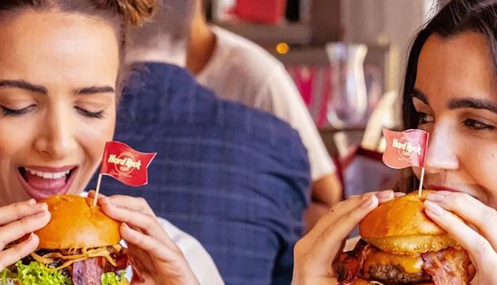 Two people are happily eating burgers with small Hard Rock Cafe flags on top