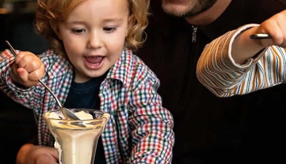 A joyful child eagerly reaches for a dessert with a spoon