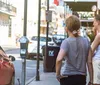 A man is speaking to a group of women on a city sidewalk near parking meters