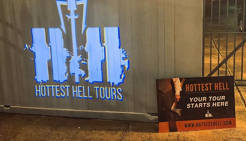 The image shows a projected logo and a sign for Hottest Hell Tours with the text Your Tour Starts Here and a website URL