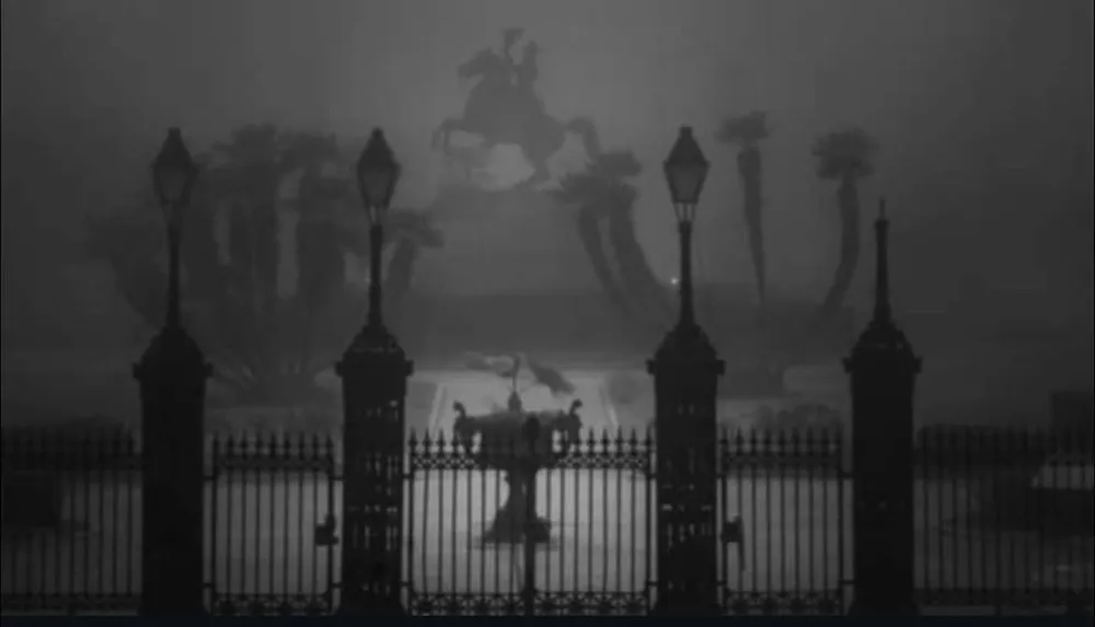 A foggy night view of a gated park featuring a silhouetted equestrian statue and palm trees in the background