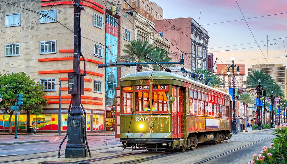 A vintage streetcar travels along a vibrant street lined with colorful buildings and palm trees at sunset