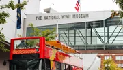 A red sightseeing bus is parked in front of The National WWII Museum.