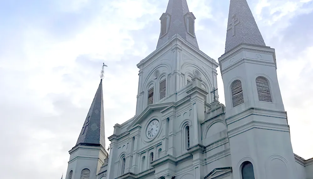 The image shows a large historic cathedral with three tall spires and a prominent clock on its facade