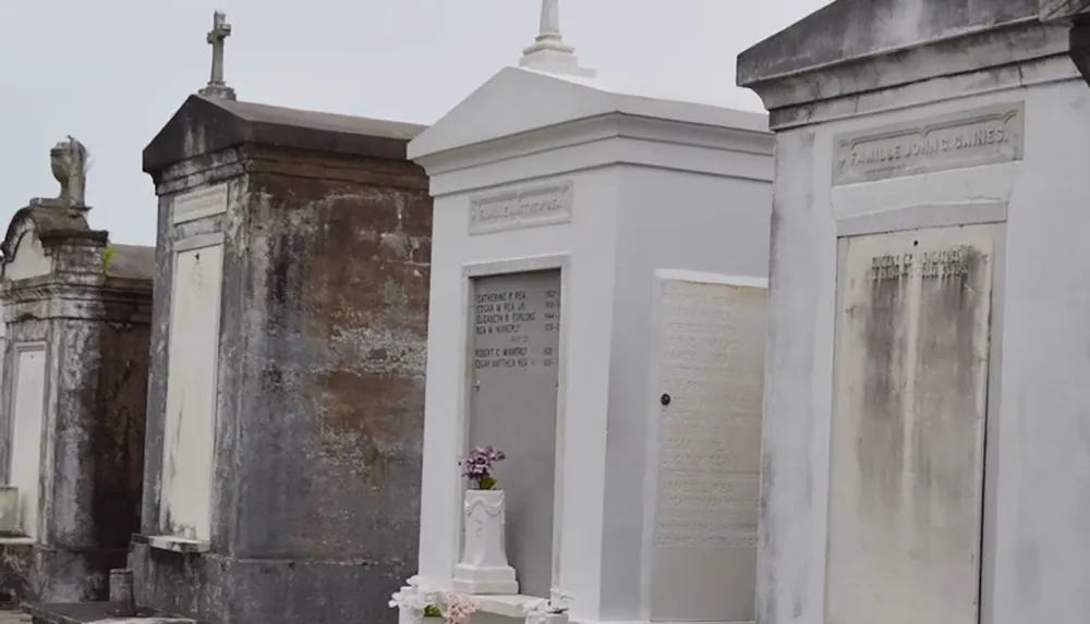 The image shows a row of above-ground tombs in a cemetery with flowers placed on the white tomb at the center