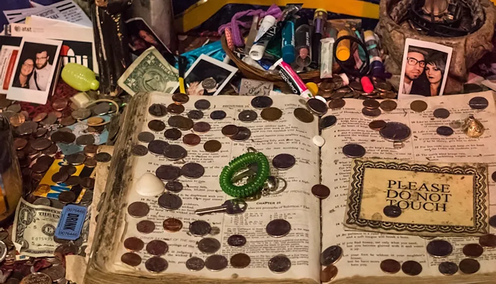 An old book is surrounded by various items like coins photos and lip balm with a sign reading PLEASE DO NOT TOUCH