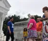 A group of people stands near a white mausoleum with one person appearing to guide or speak to the others