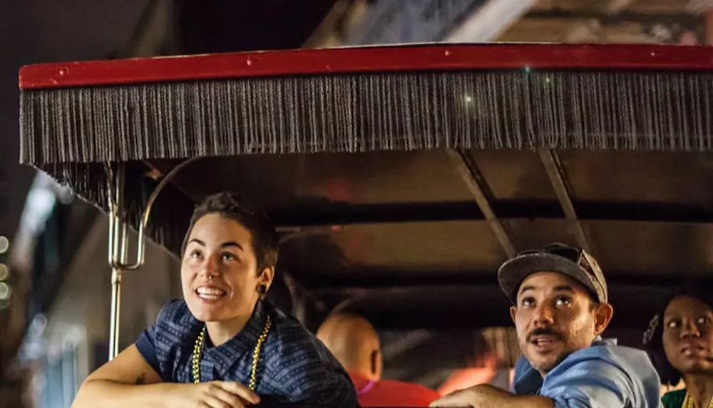 Two people are sitting in a pedicab looking upwards with interest during nighttime