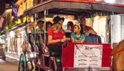 A group of people are enjoying a horse-drawn carriage ride on a lively, city street at night.