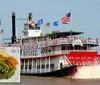 A red and white paddlewheel steamboat adorned with American flags cruises on a river churning water with its iconic red wheel