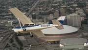 A single-engine propeller aircraft is flying over a city with a distinctive dome-shaped building below.