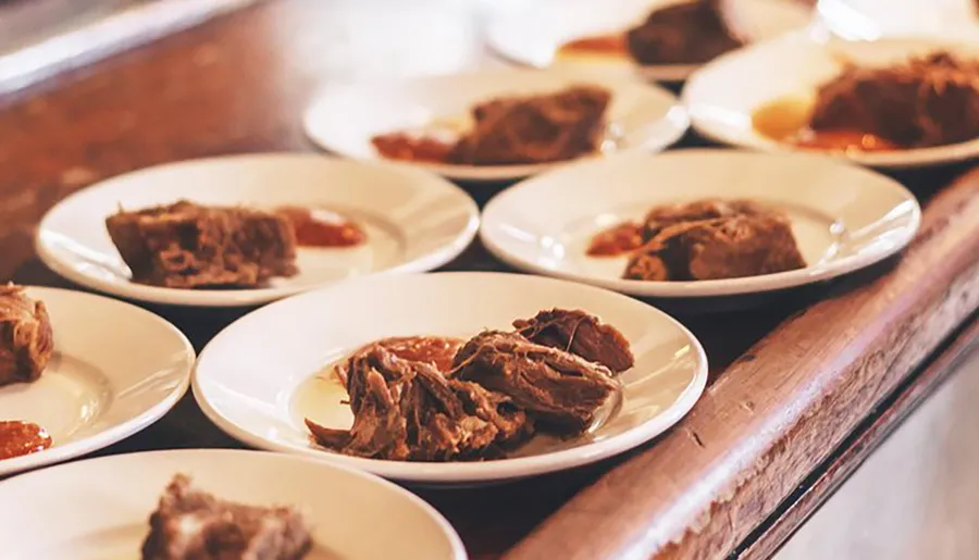 The image shows several plates with portions of meat lined up on a wooden surface, likely suggesting a food tasting event or a serving set up at a buffet.