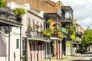 The image shows a street in the French Quarter of New Orleans, lined with historic buildings featuring iconic ironwork balconies and colorful façades.