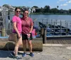 Two individuals are standing in front of a dock with an airboat and life vests in the background indicating a location likely used for boat tours