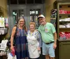 Three smiling adults are posing for a photo inside a shop with shelves displaying souvenirs and culinary products