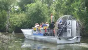 A group of people are taking a tour on an airboat through a lush, green waterway.