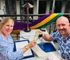 Two people are cheerfully toasting with drinks at an outdoor restaurant adorned with colorful fabrics