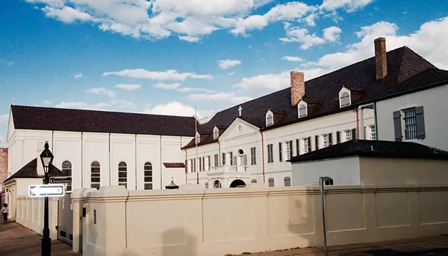 The image shows the historic Ursuline Convent in the French Quarter of New Orleans, characterized by its traditional architecture and a clear blue sky.