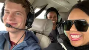 Three people are smiling for a selfie while wearing aviation headsets, seated inside what appears to be a small aircraft.