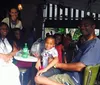 A group of people including a child are smiling and seated at a table in an outdoor dining area with a waitress standing behind them