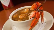 The image features a bowl of gumbo adorned with a whole crab on top, signaling a seafood-based rendition of the classic Louisiana dish.