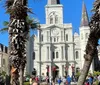 The image shows a bustling square with people walking flanked by tall palm trees with the iconic St Louis Cathedral in the background adorned with Christmas wreaths on a sunny day