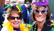 Two people are wearing Mardi Gras-themed accessories and smiling at the camera during a festive celebration.