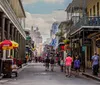The image depicts a vibrant street scene with people walking among historical buildings some adorned with flags and iron balconies in what appears to be the French Quarter of New Orleans
