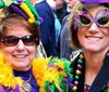 Two people are smiling for the camera wearing festive Mardi Gras attire including colorful beads and masks