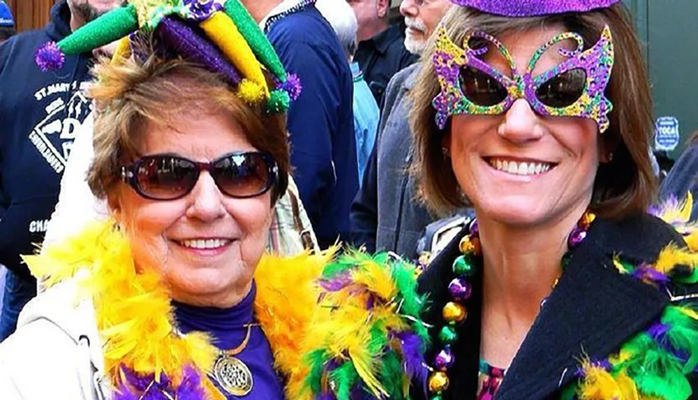 Two people are smiling for the camera wearing festive Mardi Gras attire including colorful beads and masks