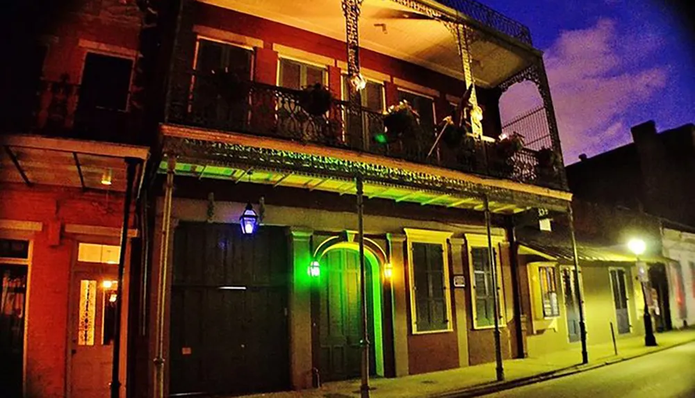 A vibrant street scene at night showing a traditional building with a wrought iron balcony illuminated by green and blue lights