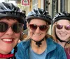 Three smiling individuals wearing bike helmets and sunglasses are posing for a selfie on a city street