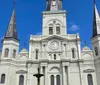 The image shows the historic Cabildo building with its iconic French colonial architecture located next to St Louis Cathedral in Jackson Square New Orleans behind an ornate iron fence with tropical foliage framing the view