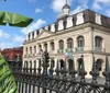 The image shows the historic Cabildo building with its iconic French colonial architecture located next to St Louis Cathedral in Jackson Square New Orleans behind an ornate iron fence with tropical foliage framing the view