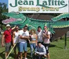 A group of people is posing with smiles in front of the Jean Lafitte Swamp Tours sign featuring a large cartoon alligator