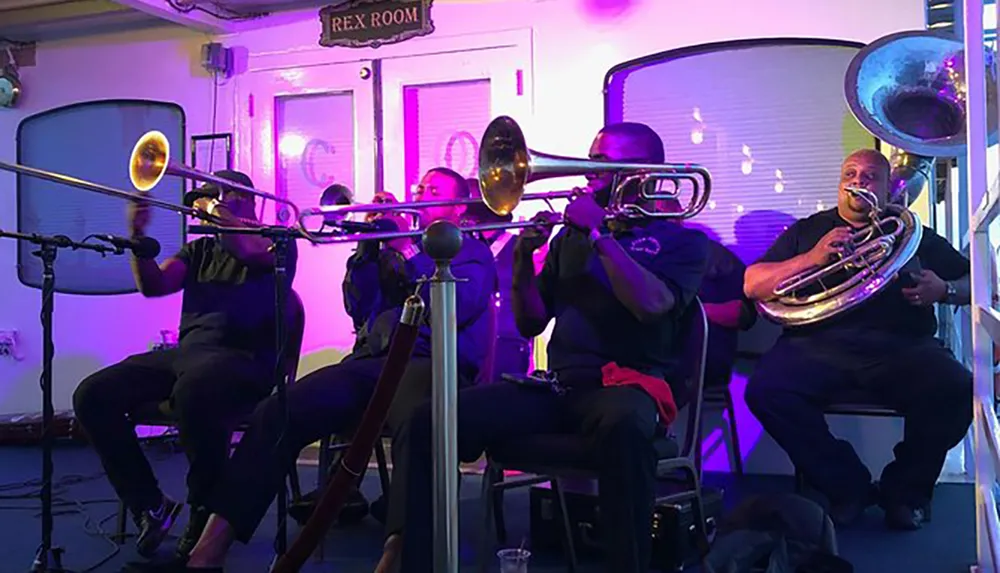 A brass band with trombones and a tuba is performing on a small lit stage designated as the REX ROOM