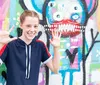 A smiling girl is posing with her hands up in front of a vibrant graffiti wall