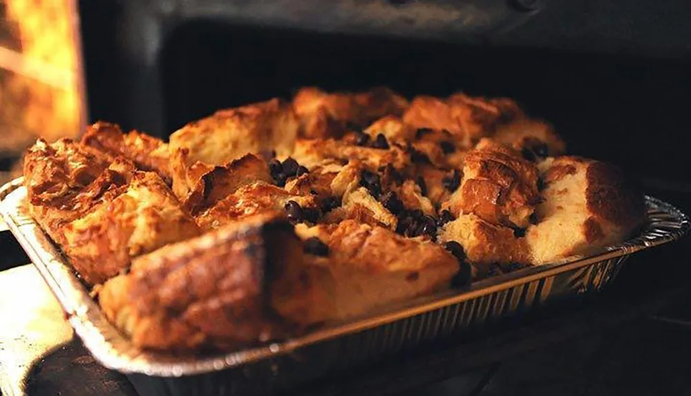 A tray of freshly baked bread pudding with raisins is coming out of the oven